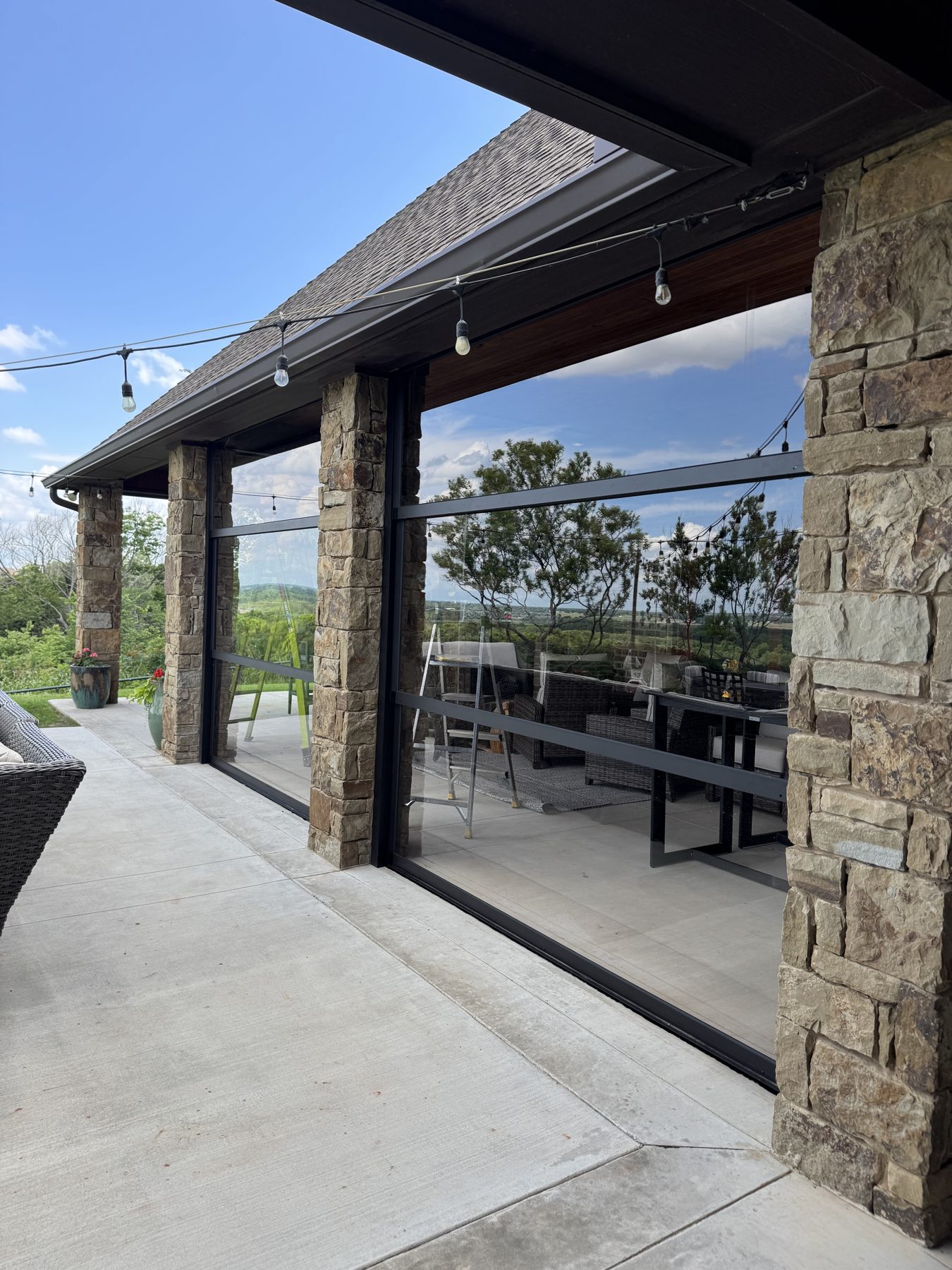 Stone-column covered patio with a Stax motorized screen system open to a hillside view